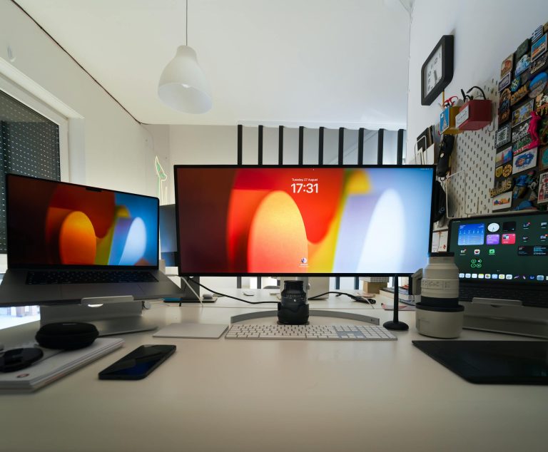 A sleek home office setup featuring multiple screens, laptops, and camera lenses on a white desk.