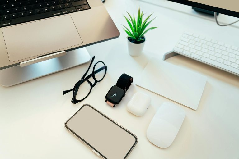 Overhead view of a sleek workspace with a laptop, smartphone, smartwatch, and tech accessories.